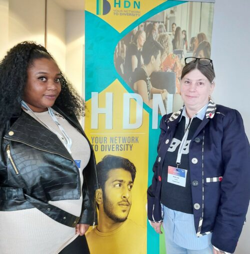 Two Greatwell Homes customers stand either side of a sign promoting the Housing Diversity Network conference